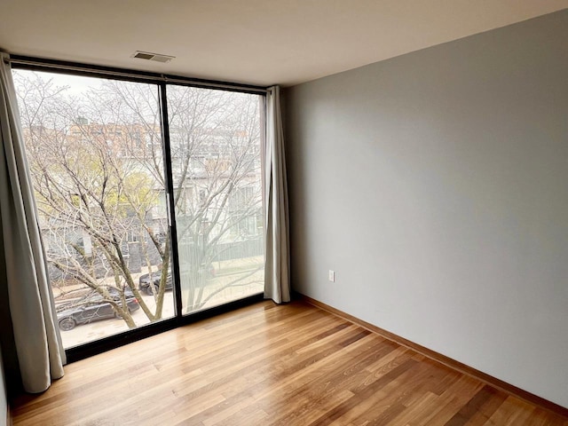 unfurnished room with visible vents, baseboards, a wall of windows, and light wood finished floors