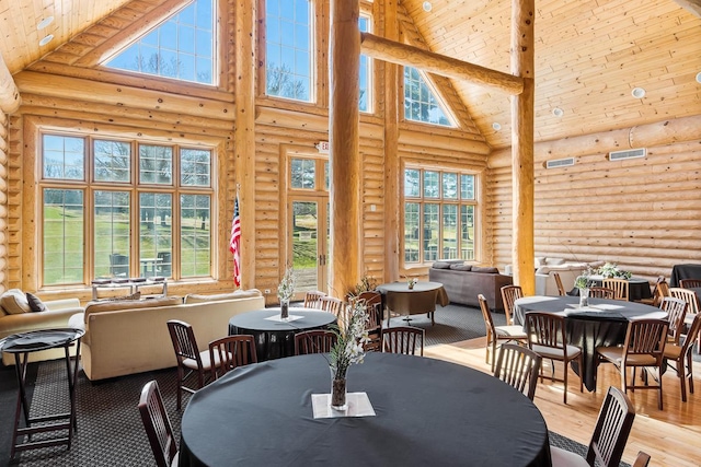 dining room with wood finished floors, a healthy amount of sunlight, log walls, and high vaulted ceiling