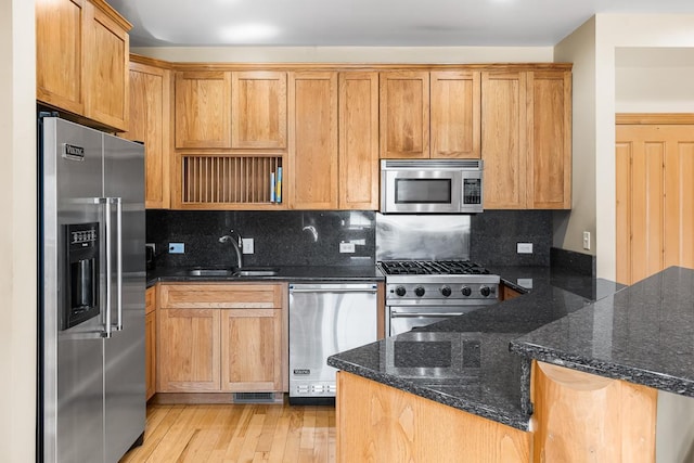 kitchen with high end appliances, a sink, dark stone counters, a peninsula, and light wood-style flooring