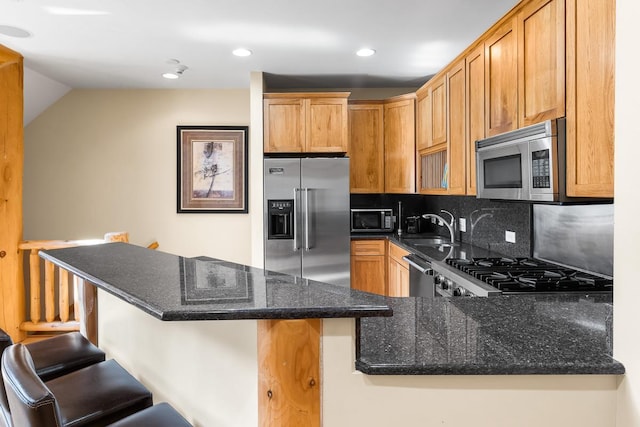 kitchen with dark stone countertops, a sink, decorative backsplash, stainless steel appliances, and a kitchen bar