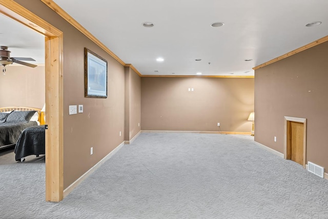 below grade area featuring carpet, visible vents, crown molding, baseboards, and ceiling fan