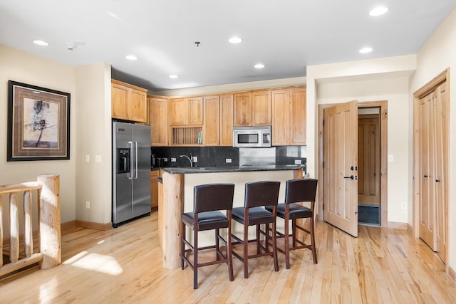 kitchen with light wood-style flooring, a kitchen bar, appliances with stainless steel finishes, and tasteful backsplash