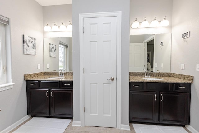 bathroom featuring two vanities, baseboards, and a sink