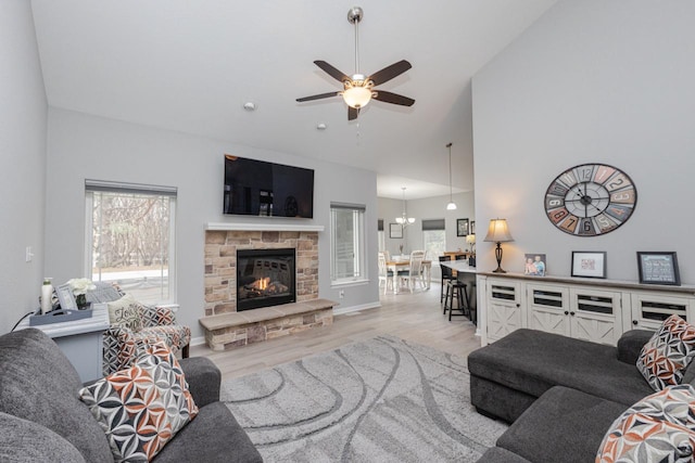 living area with light wood finished floors, a stone fireplace, high vaulted ceiling, and ceiling fan