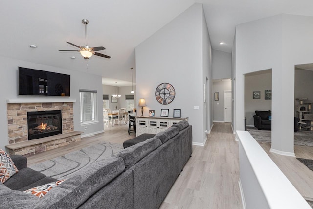 living area featuring high vaulted ceiling, a ceiling fan, a stone fireplace, light wood-style floors, and baseboards