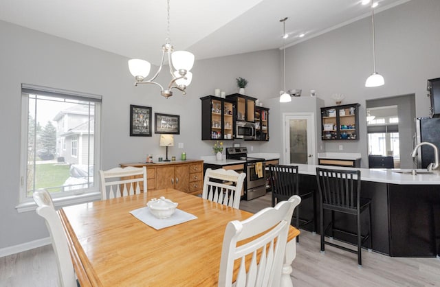 dining space with light wood-style floors, a wealth of natural light, high vaulted ceiling, and an inviting chandelier