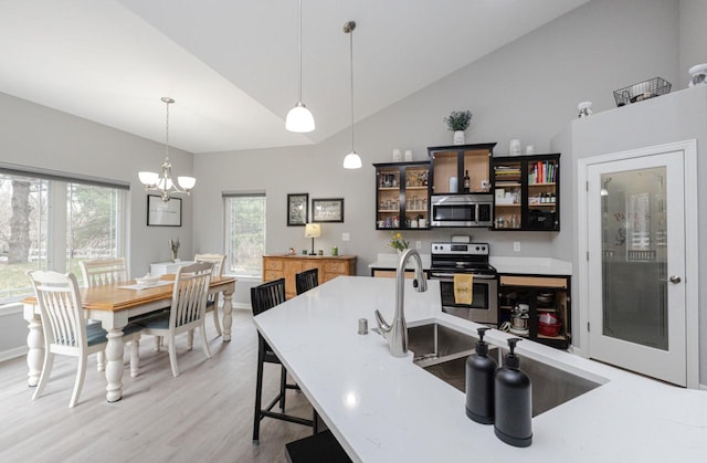 kitchen featuring glass insert cabinets, light wood-style flooring, pendant lighting, and appliances with stainless steel finishes
