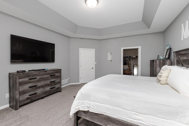 carpeted bedroom with a tray ceiling, a closet, a spacious closet, and baseboards