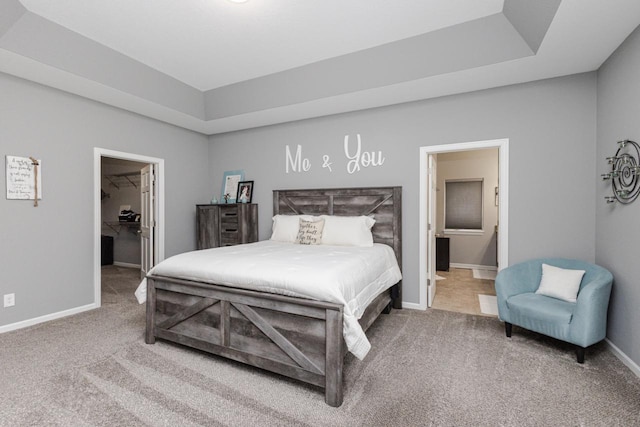 bedroom featuring a walk in closet, a raised ceiling, carpet floors, and baseboards