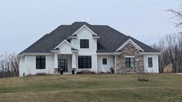 view of front of property with board and batten siding, roof with shingles, stone siding, and a front yard