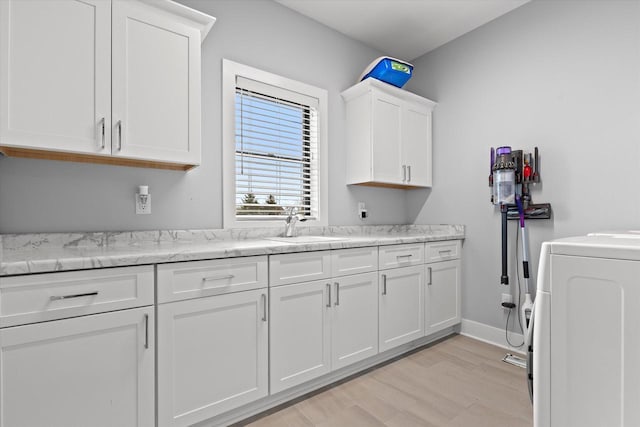 kitchen with a sink, light stone counters, white cabinets, washer / dryer, and light wood-style flooring