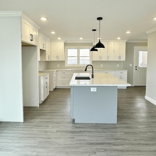 kitchen with ornamental molding, a sink, a center island with sink, light wood-style flooring, and white cabinetry