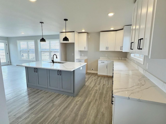 kitchen with light stone counters, gray cabinets, a sink, light wood-type flooring, and baseboards