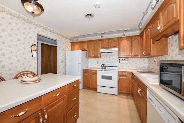 kitchen featuring white appliances, wallpapered walls, under cabinet range hood, light countertops, and brown cabinets