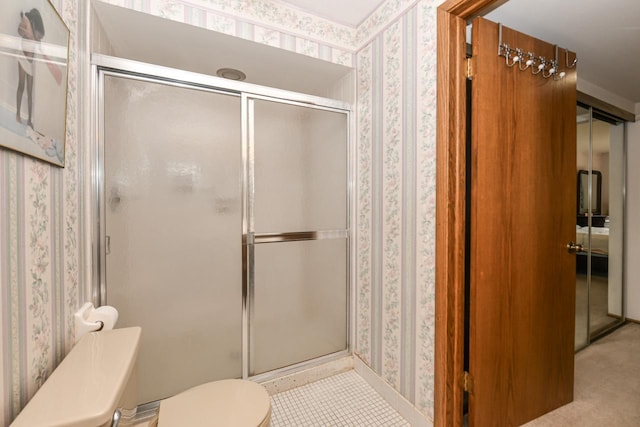 bathroom with toilet, a shower stall, and wallpapered walls