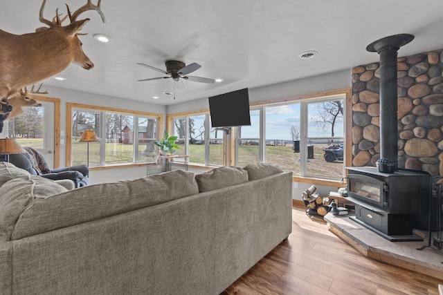 living room featuring wood finished floors, a wood stove, a wealth of natural light, and ceiling fan