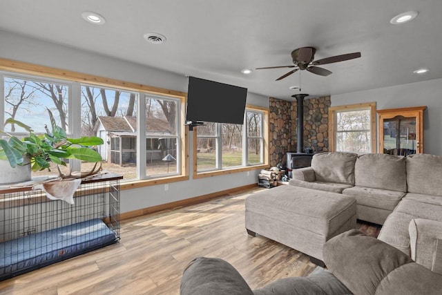living room with a wealth of natural light, visible vents, baseboards, a ceiling fan, and a wood stove