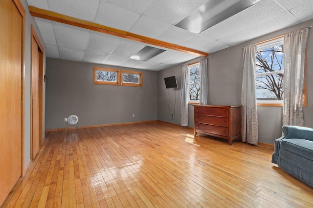 basement with baseboards, a paneled ceiling, and light wood-style flooring