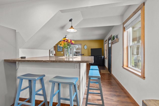 kitchen with dark wood finished floors, a breakfast bar, decorative light fixtures, baseboards, and a peninsula
