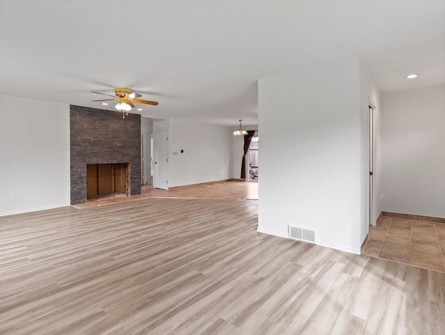 4155 Finch Ln, Delavan, WI 53115 - unfurnished living room featuring light wood-type flooring, baseboards, visible vents, ceiling fan with notable chandelier, and a large fireplace