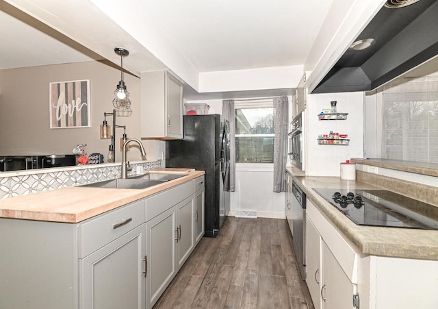 kitchen with a peninsula, dark wood-style floors, a sink, decorative light fixtures, and black appliances