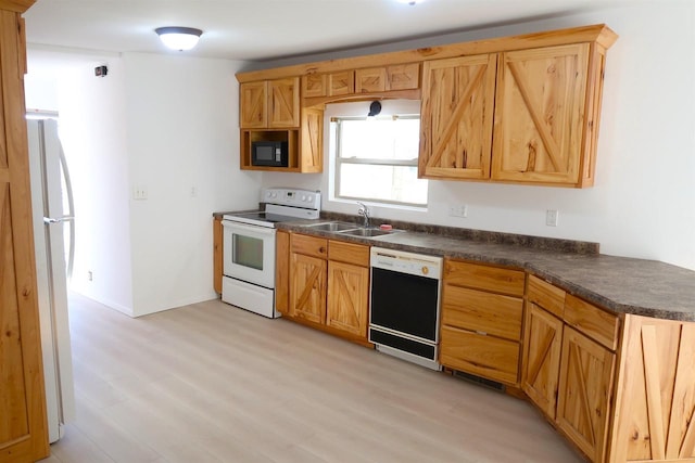 kitchen featuring light wood-type flooring, dark countertops, white appliances, and a sink