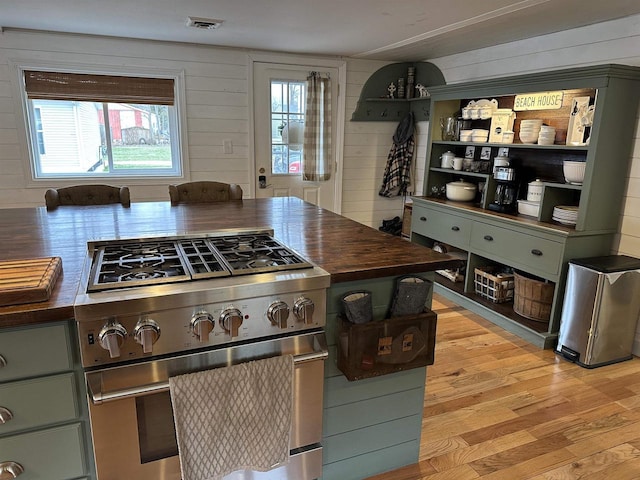 kitchen with light wood-style flooring, visible vents, high end stove, butcher block counters, and wooden walls