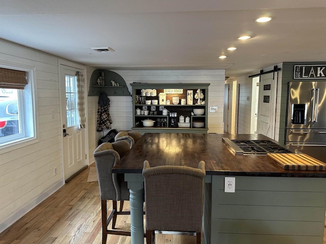 bar with a barn door, light wood-style flooring, wooden walls, and stainless steel fridge
