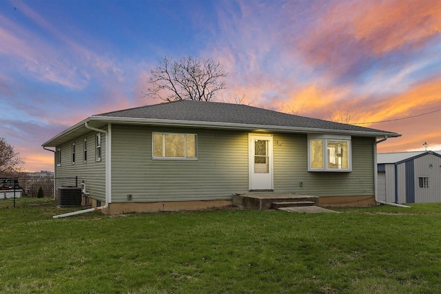 back of house at dusk featuring fence, an outbuilding, a yard, and a storage unit