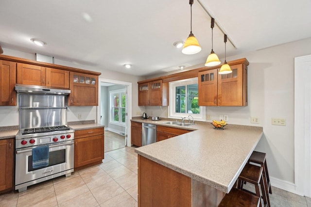 5407 Marsh Woods Dr, Mcfarland, WI 53558 - kitchen featuring appliances with stainless steel finishes, under cabinet range hood, brown cabinets, a breakfast bar, and a sink