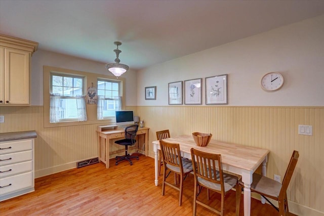 dining area with light wood finished floors, a wainscoted wall, and baseboards