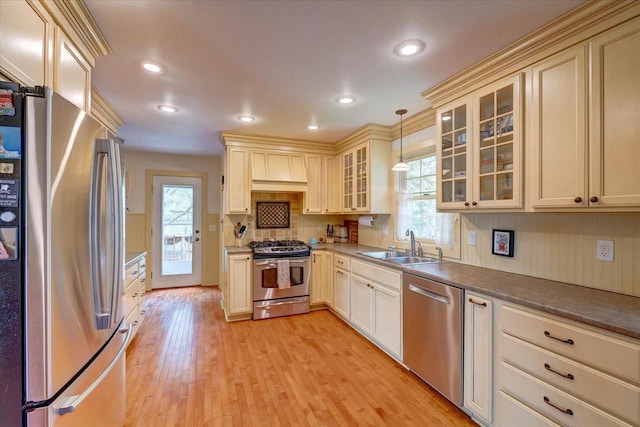 kitchen featuring a sink, stainless steel appliances, light wood-type flooring, cream cabinetry, and decorative light fixtures