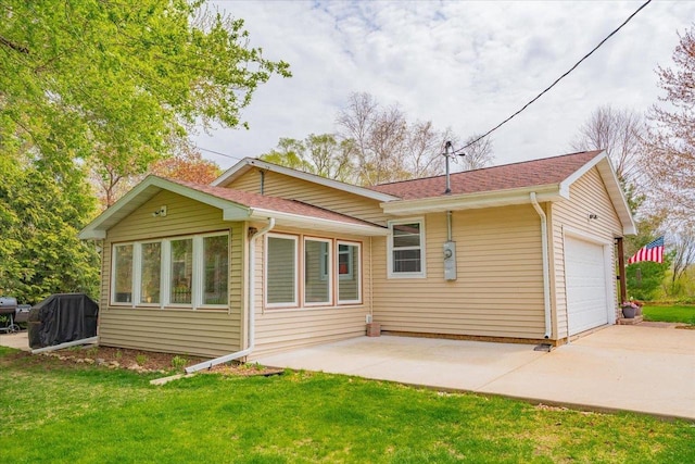 rear view of house with concrete driveway, a yard, and an attached garage