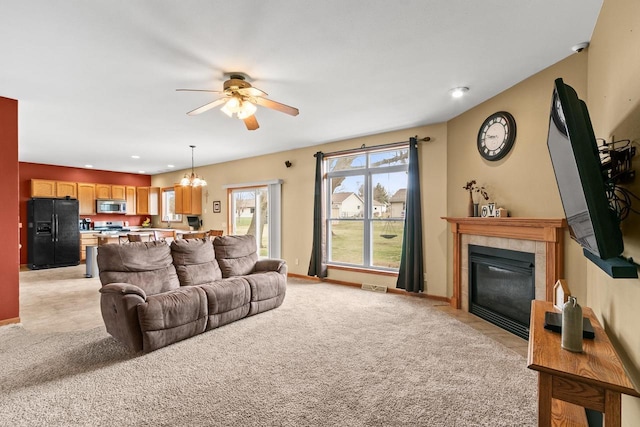 living area with ceiling fan with notable chandelier, visible vents, a fireplace, and light colored carpet
