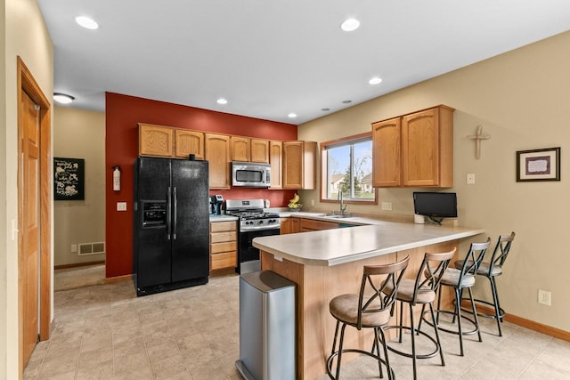 kitchen featuring a kitchen breakfast bar, light countertops, a sink, a peninsula, and appliances with stainless steel finishes