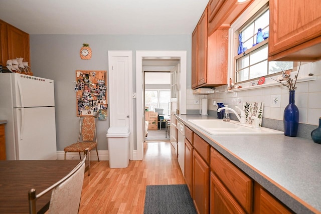 kitchen featuring brown cabinets, backsplash, a sink, white appliances, and light wood-type flooring