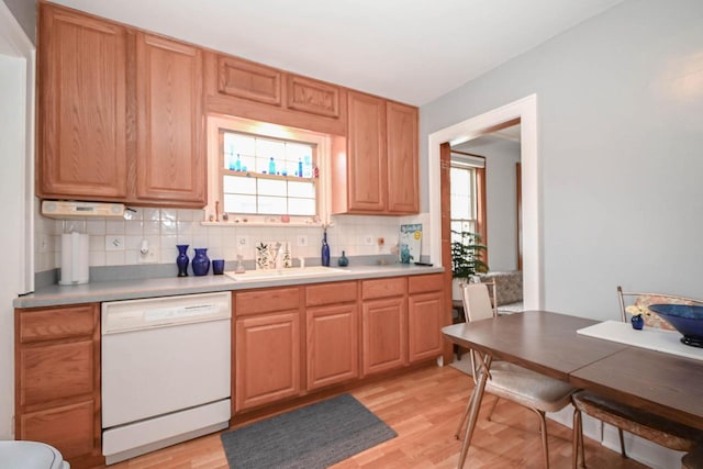 kitchen with light wood finished floors, a healthy amount of sunlight, a sink, white dishwasher, and decorative backsplash