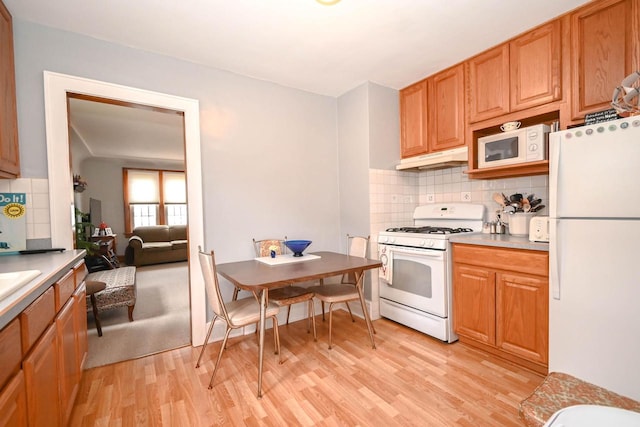 kitchen with light wood finished floors, under cabinet range hood, white appliances, and decorative backsplash