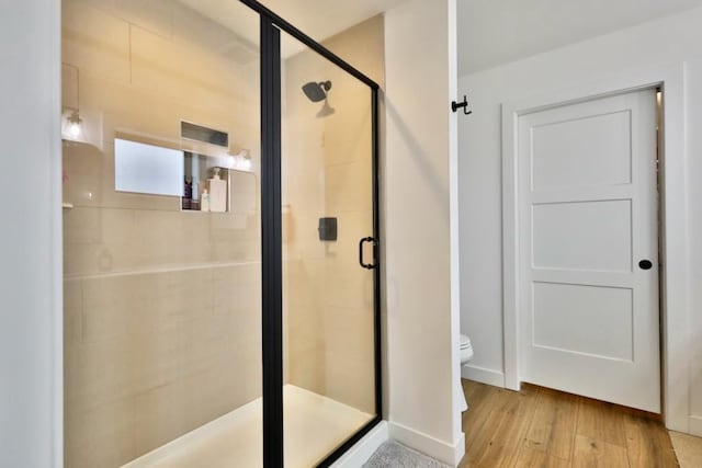 bathroom with baseboards, wood finished floors, a shower stall, and toilet