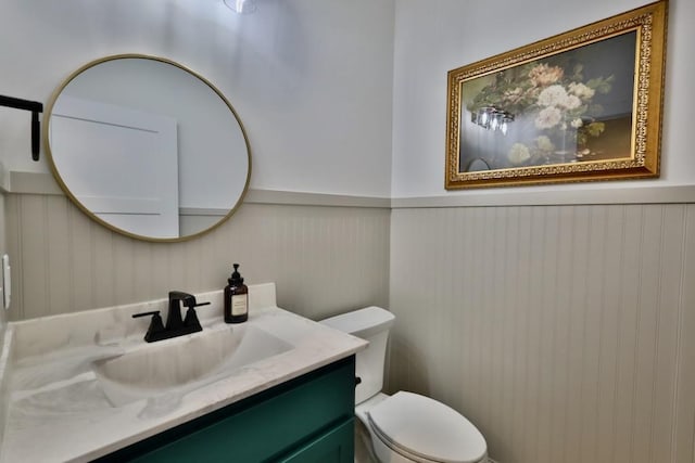 half bathroom featuring toilet, vanity, and wainscoting