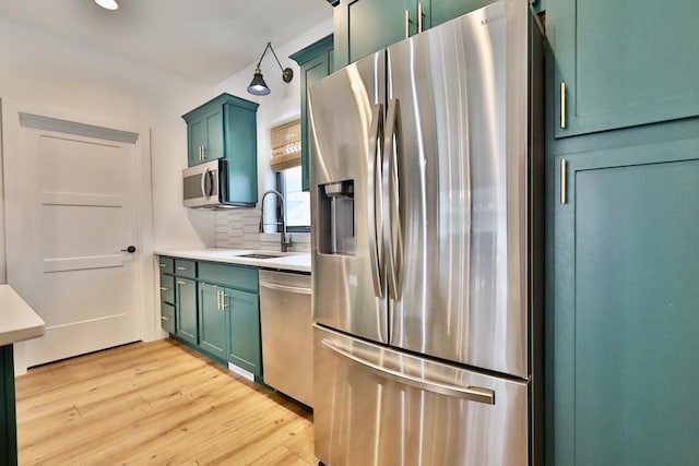 kitchen with a sink, decorative backsplash, appliances with stainless steel finishes, light wood-style flooring, and green cabinetry