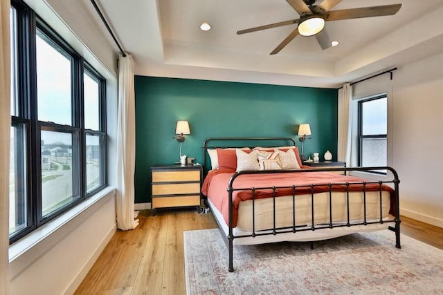 bedroom featuring hardwood / wood-style flooring, baseboards, a tray ceiling, and recessed lighting