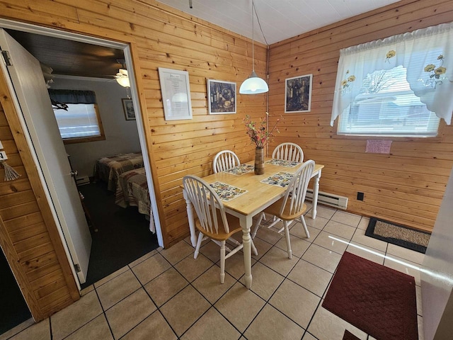 dining area with a baseboard radiator, a ceiling fan, wooden walls, and light tile patterned floors