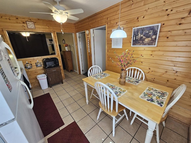 dining area featuring light tile patterned flooring, wood walls, and ceiling fan