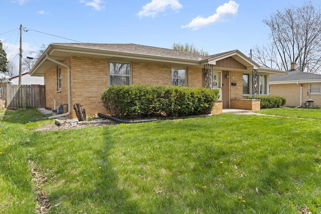 ranch-style home with brick siding, fence, a shingled roof, and a front lawn
