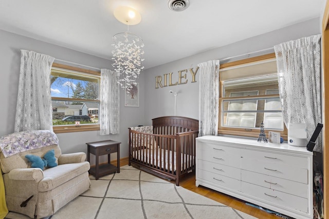 bedroom with a crib, a chandelier, light wood-style flooring, and visible vents