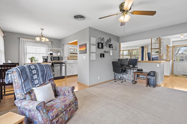 living area featuring visible vents, baseboards, ceiling fan with notable chandelier, and light carpet