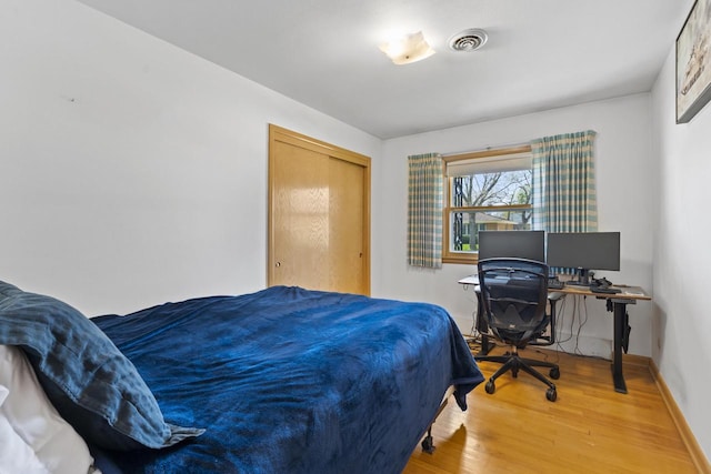 bedroom with baseboards, visible vents, light wood-style flooring, and a closet