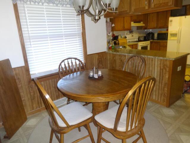 545 Skyhawk Ave, Campbellsport, WI 53010 - dining space featuring an inviting chandelier, wainscoting, wooden walls, and light floors
