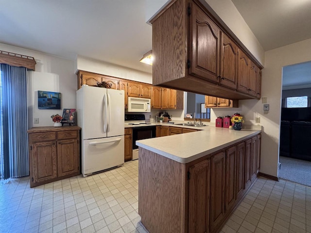 kitchen with brown cabinets, light countertops, a sink, white appliances, and a peninsula